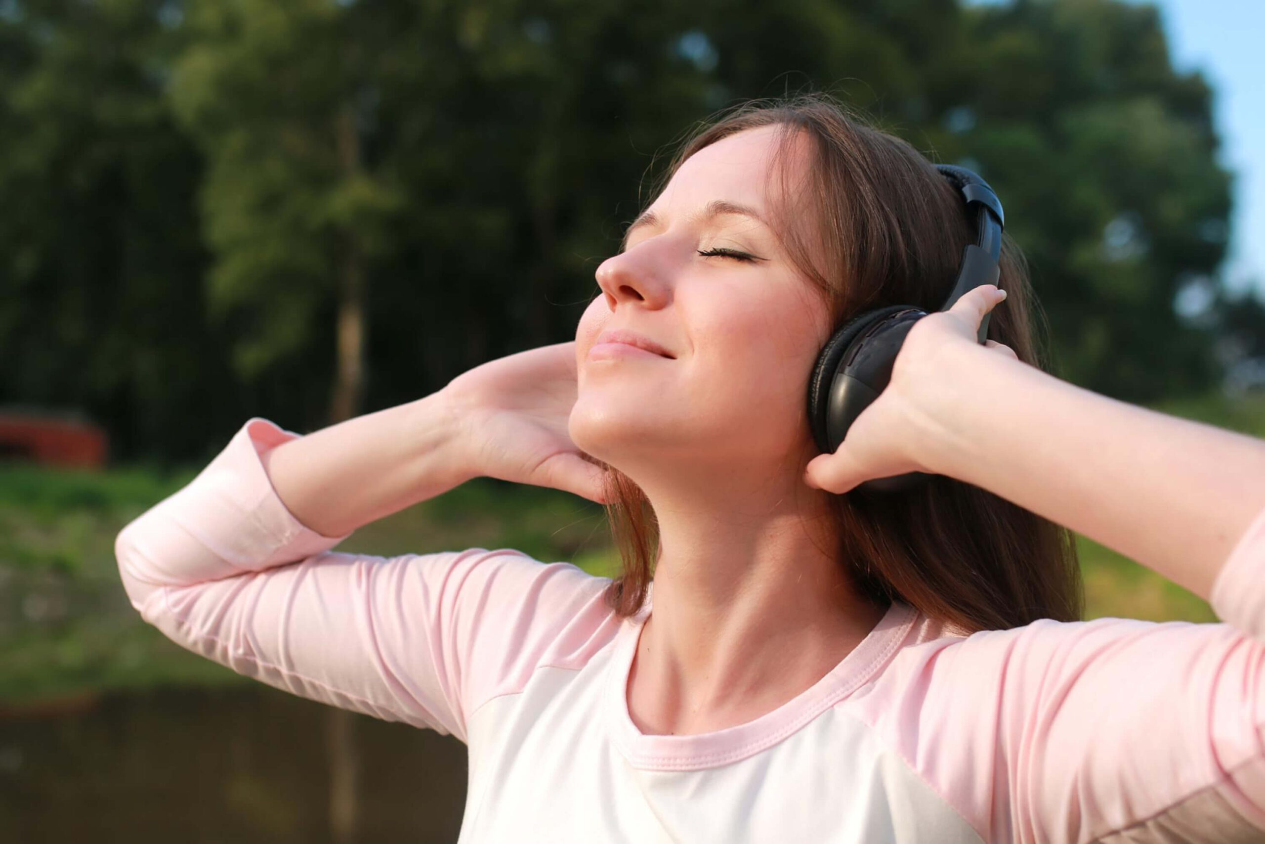 Lady smiling with her eyes closed facing the sun while wearing headphones :Headphone Tour
